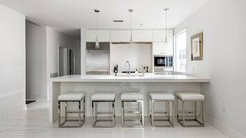 A modern kitchen with a large island, bar stools, pendant lights, and a microwave.