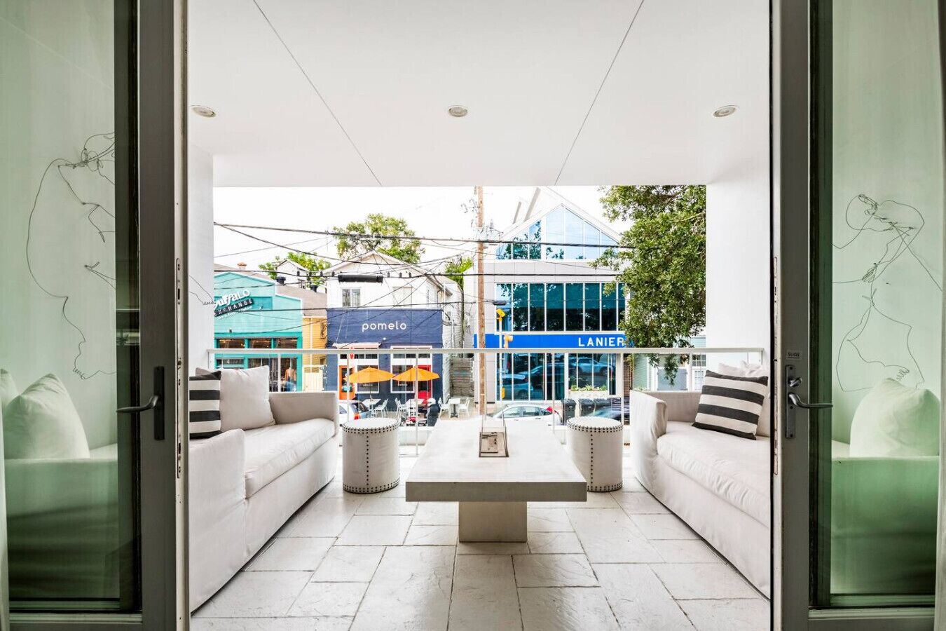 An open-plan living area with a sofa set, a coffee table, and a view of the street with shops.