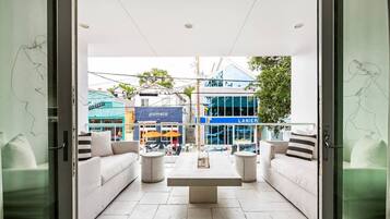 An open-plan living area with a sofa set, a coffee table, and a view of the street with shops.
