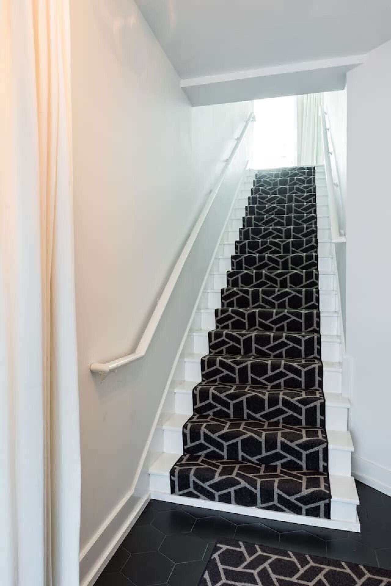 A staircase with a geometric patterned carpet and white walls.