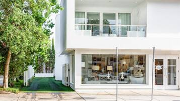 A modern two-story building with a glass facade, a visible interior with furniture, and a green lawn in front.