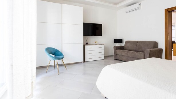 Un dormitorio con cama, televisión, sofá, sillón y armario.