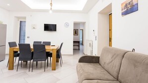 Un espacio habitable moderno con comedor, un sofá, un televisor y un reloj en la pared.