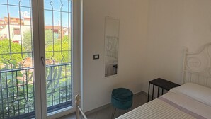 Un dormitorio con cama, un taburete pequeño, una mesita de noche y vistas a través de un ventanal corredero.