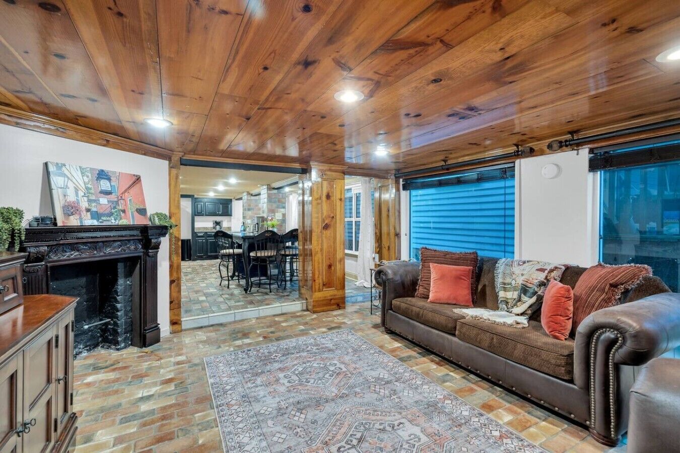 A living room with a fireplace, a sofa, a rug, and a view of the kitchen.