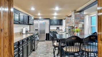 A kitchen with dark cabinets, a stainless steel refrigerator, a granite countertop, and a dining area with a table and chairs.