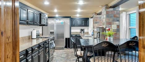 A kitchen with dark cabinets, a stainless steel refrigerator, a granite countertop, and a dining area with a table and chairs.