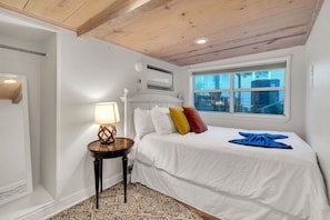 Ein Schlafzimmer mit einem Bett, einer Nachttischlampe, einem Fenster und einem gemusterten Teppich.