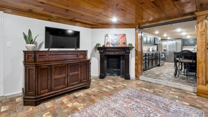 Una sala de estar con chimenea, televisor y cocina visible a través de un umbral abierto.