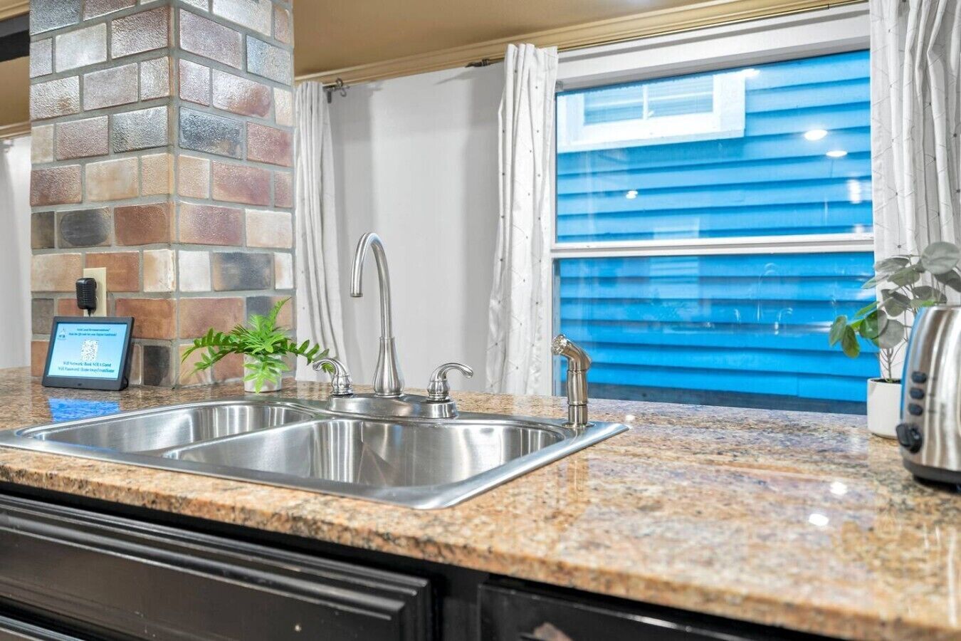 A kitchen with a granite countertop, stainless steel sink, and a brick accent wall.