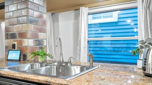 Una cocina con encimera de granito, pileta de acero inoxidable y una pared decorativa de ladrillo.