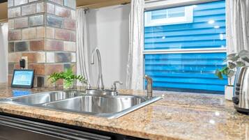 A kitchen with a granite countertop, stainless steel sink, and a brick accent wall.