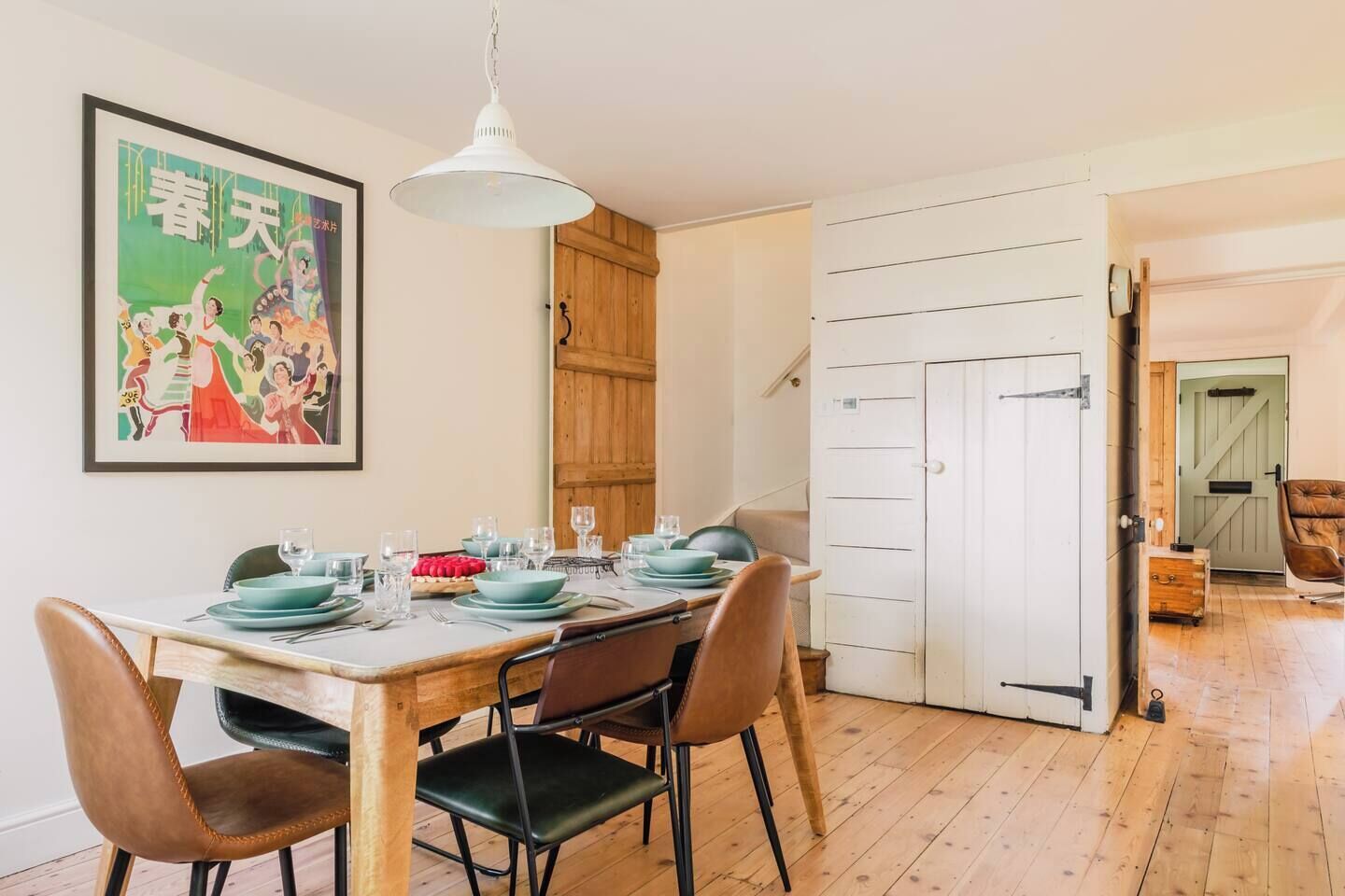 Un comedor con una mesa de madera dispuesta para cuatro personas, una lámpara colgante y una puerta que da a otra habitación.