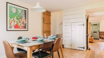 Un comedor con una mesa de madera dispuesta para cuatro personas, una lámpara colgante y una puerta que da a otra habitación.