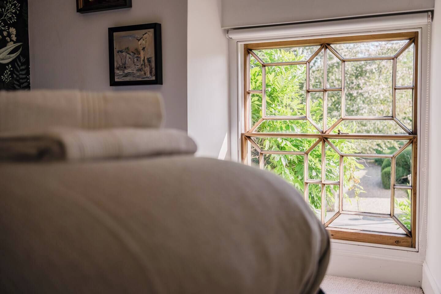 A bedroom with a large bed, a window with a geometric design, and a framed picture on the wall.
