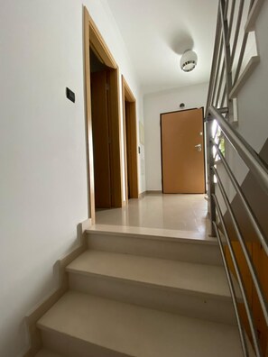 Eine Treppe führt zu einer Tür, mit einer Handlauf auf der rechten Seite und einer Deckenleuchte.