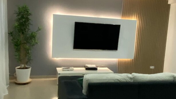 Ett modernt hotellrum med en platt-TV som är monterad på väggen, en soffa, ett litet bord och en krukväxt.