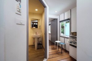 A narrow hallway with a wooden floor, a white sink with a mirror, and a small stool. - The Jewelry · The Boutique Favorite (Bang Rak)