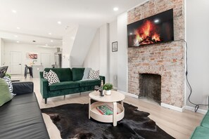 Una sala de estar moderna con un sofá verde, una mesa de centro redonda, una chimenea y un televisor de pantalla plana montado encima.