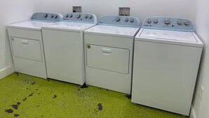 Une rangée de quatre machines à laver Whirlpool dans une buanderie, le sol étant recouvert d’un revêtement vert à motifs.