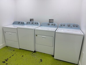 Une rangée de quatre machines à laver Whirlpool dans une buanderie, le sol étant recouvert d’un revêtement vert à motifs.