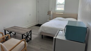 Une chambre à coucher comprenant un lit, une table de chevet, une lampe, une fenêtre et un bureau avec une chaise.