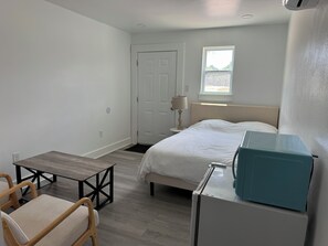 Une chambre à coucher comprenant un lit, une table de chevet, une lampe, une fenêtre et un bureau avec une chaise.