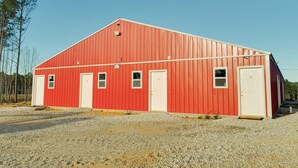 Une grange rouge avec deux portes et des fenêtres, entourée de gravier.