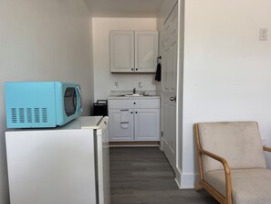 A compact kitchen with a microwave, a washing machine, and a chair.