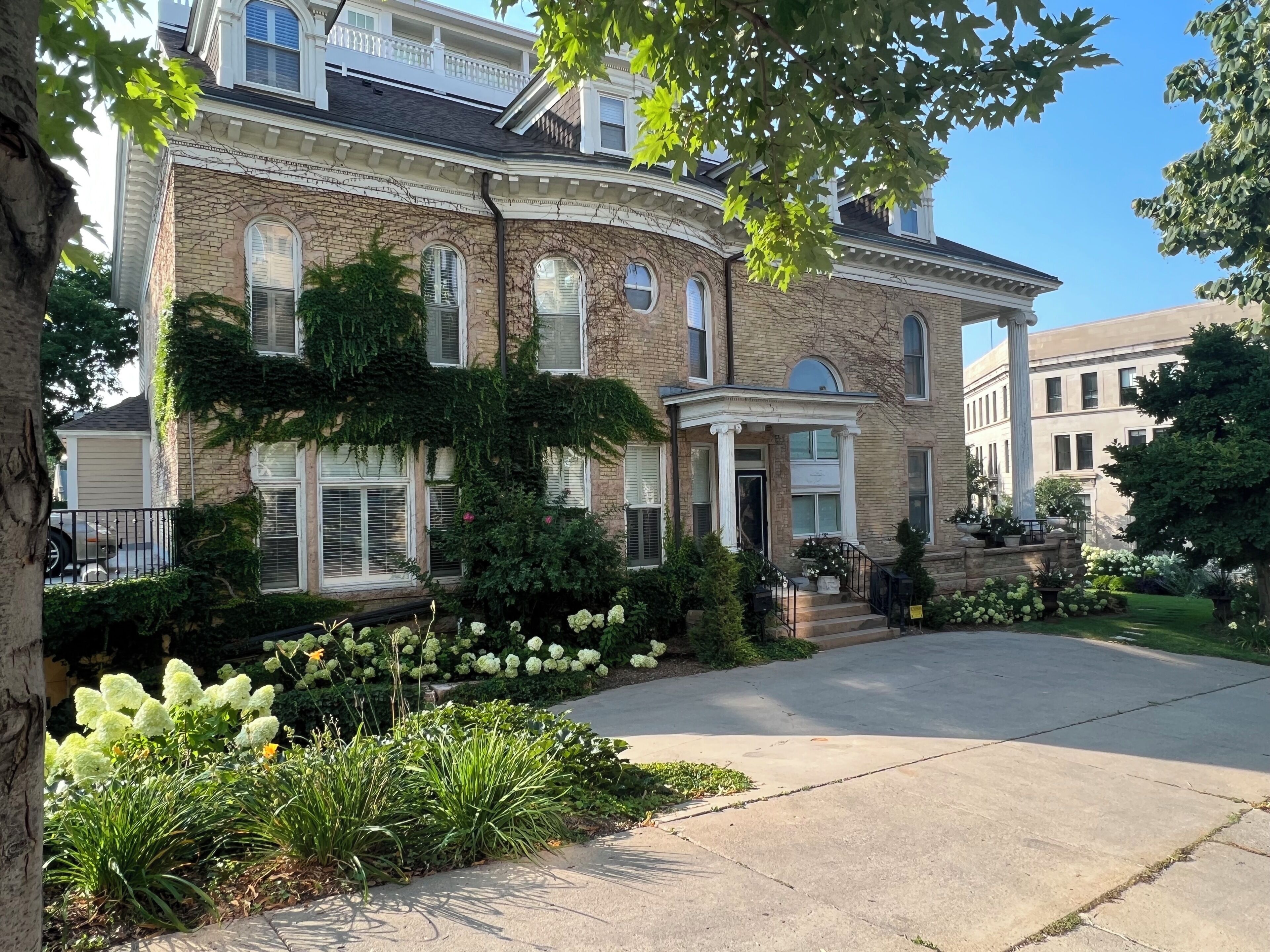 A large brick building with a central entrance, a covered porch, and a well-maintained garden with various plants and flowers.