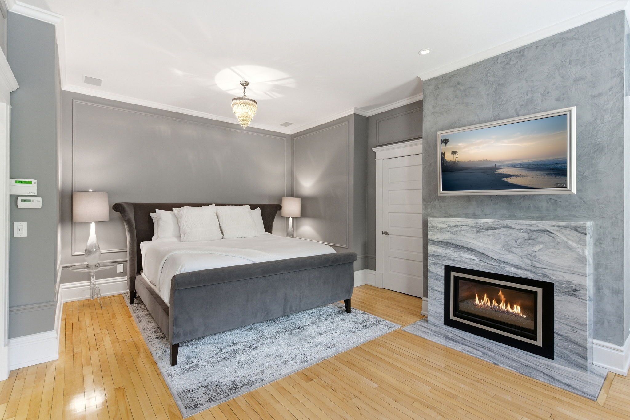 A bedroom with a bed, bedside lamps, a fireplace, a framed picture, and a ceiling light.