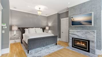 A bedroom with a bed, bedside lamps, a fireplace, a framed picture, and a ceiling light.