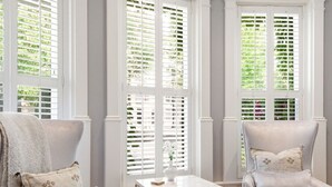 A room with a wooden floor, two armchairs, a small table, and large windows with shutters. - Villa Bella (Minneapolis)