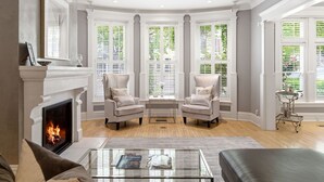 A living room with a fireplace, two armchairs, a coffee table, and large windows with shutters. - Villa Bella (Minneapolis)