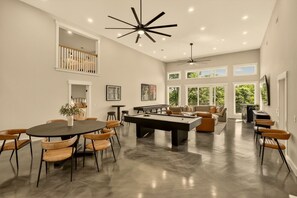A spacious living area with a pool table, comfortable seating, and large windows offering natural light.