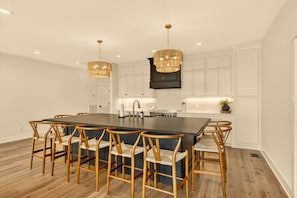 Une cuisine moderne dotée d’un îlot central, de chaises en bois, de luminaires suspendus et de meubles de rangement blancs.