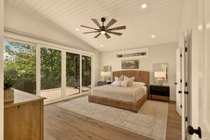 A bedroom with a large bed, a ceiling fan, a nightstand, a lamp, a painting on the wall, and a sliding glass door leading to a balcony.