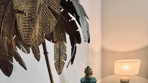 Et værelse med trægulv, et marmorbord, en dekorativ gulvlampe med fjerdesign og en lille bordlampe.