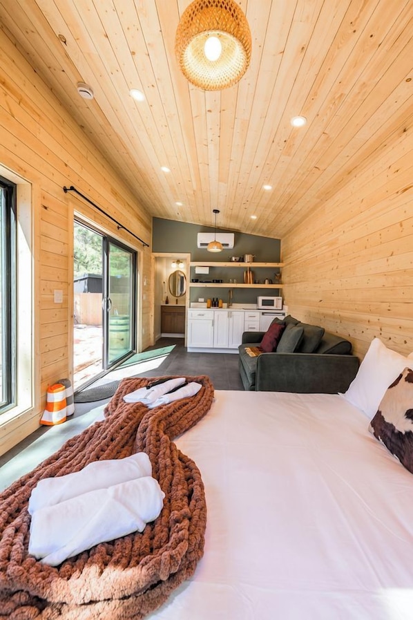 Una habitación acogedora con una cama, un sofá, kitchenette y un ventanal grande.