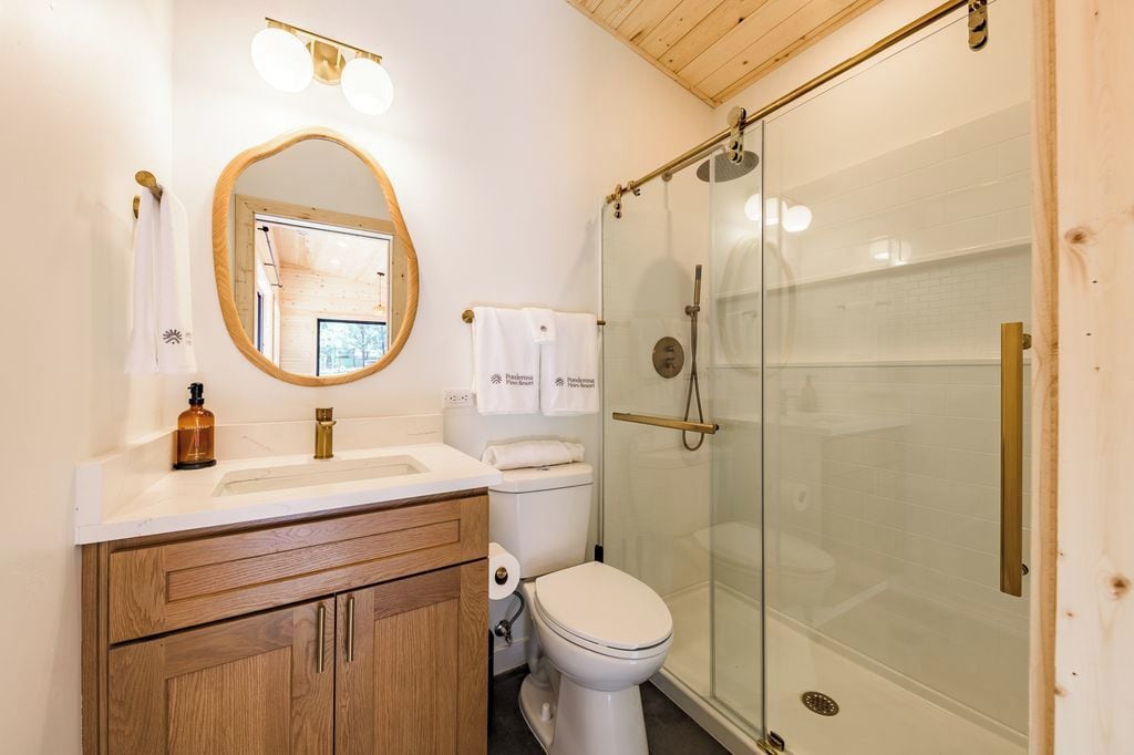 A bathroom with a wooden vanity, a toilet, a glass shower enclosure, and a mirror with a wooden frame.