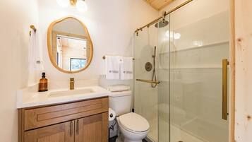 A bathroom with a wooden vanity, a toilet, a glass shower enclosure, and a mirror with a wooden frame.