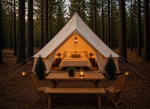 Eine Zelthotelunterkunft mit Bett, Nachttischen und einem Tisch mit Stühlen in einer Waldlandschaft.