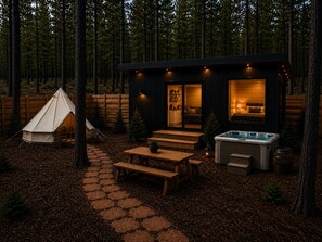 A cabin with a tent, wooden deck, hot tub, and a cozy interior with a sofa and kitchen area. - Ponderosa Pines Resort (Parks)