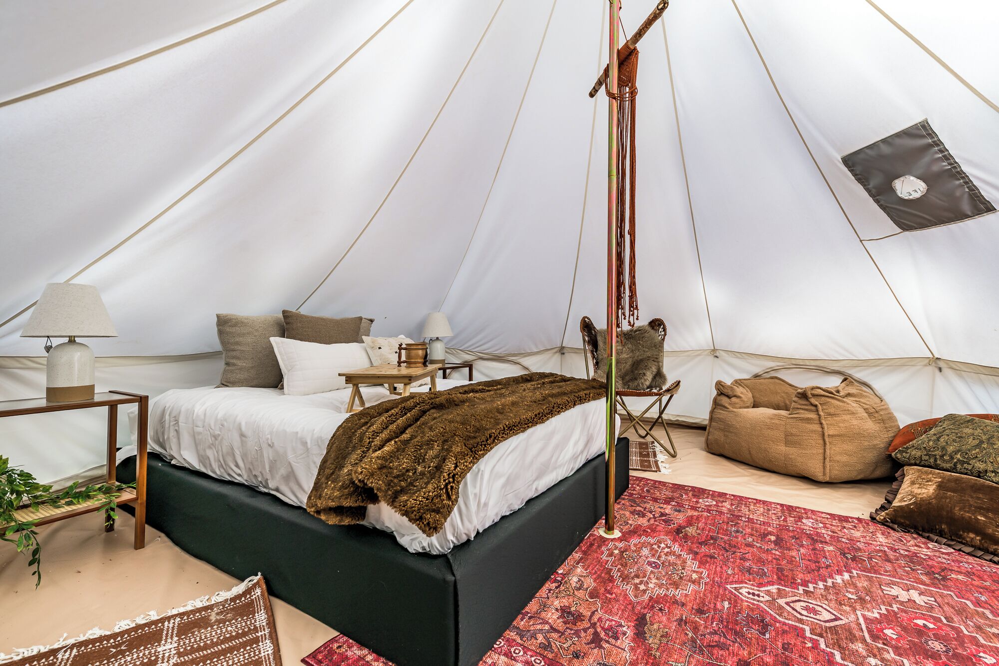 Un hébergement sous tente comprenant un lit, une petite table, une chaise et un tapis rouge à motifs.