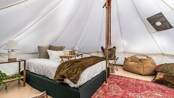 Un hébergement sous tente comprenant un lit, une petite table, une chaise et un tapis rouge à motifs.