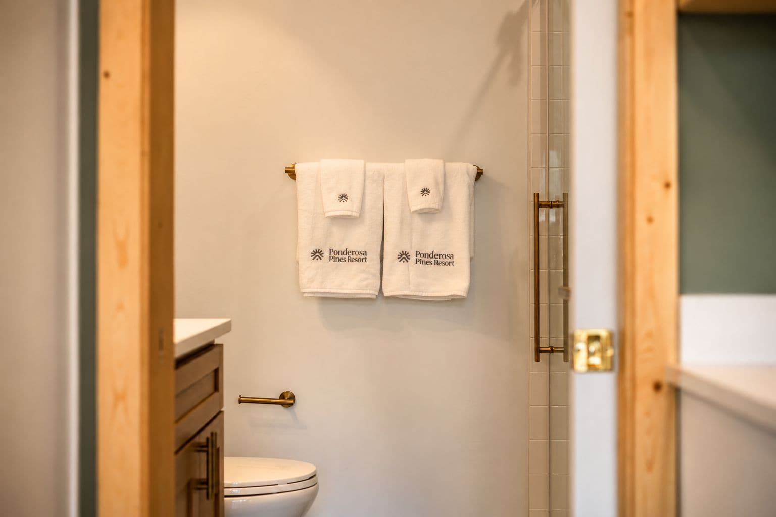 Un baño con inodoro, lavamanos y dos toallas colgadas en un perchero.