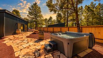 Un espace extérieur aménagé avec un jacuzzi, un sol en pierre, des tonneaux en bois et une clôture en bois.