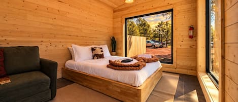 A wooden cabin bedroom with a bed, a sofa, and a large window.