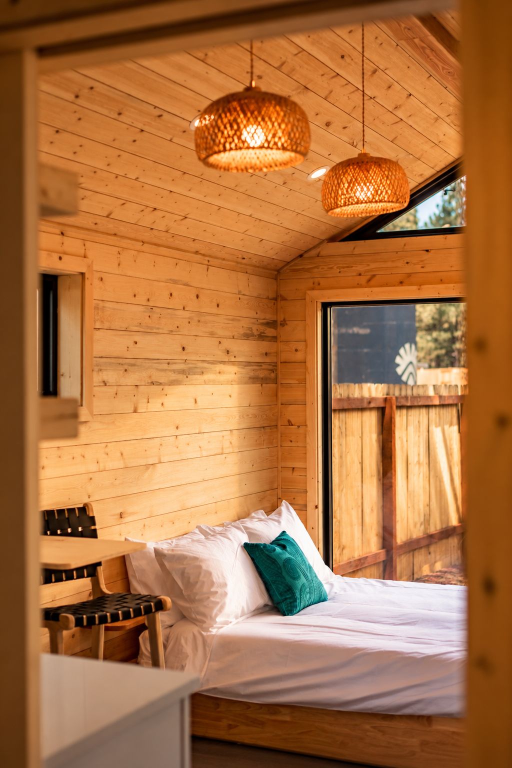 A wooden cabin interior with a bed, a table, and two hanging lamps.