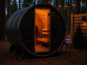 Eine holzverkleidete, fassförmige Hütte mit offener Tür, einer Bank im Inneren und einem kleinen Tisch mit Handtüchern davor.